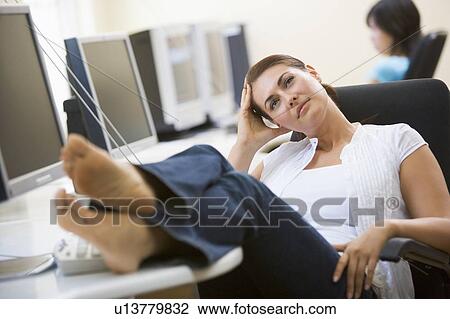 Stock Image - Woman in computer room with feet up thinking. Fotosearch