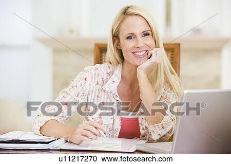 Stock Image - Woman in dining room with laptop frowning. Fotosearch