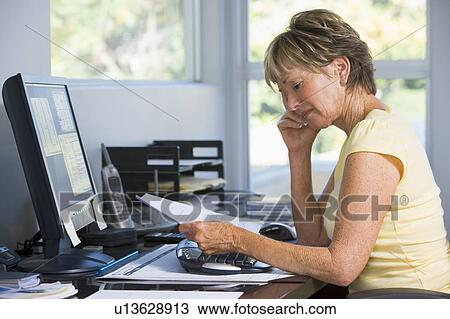 Stock Image - Woman in home office with computer and paperwork. Fotosearch