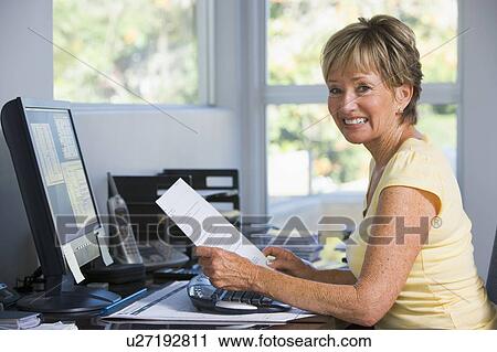 Stock Image - Woman in home office with computer and paperwork smiling. Fotosearch