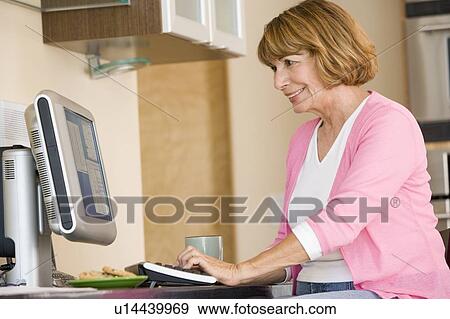 Stock Photo - Woman in kitchen with computer and coffee smiling. Fotosearch