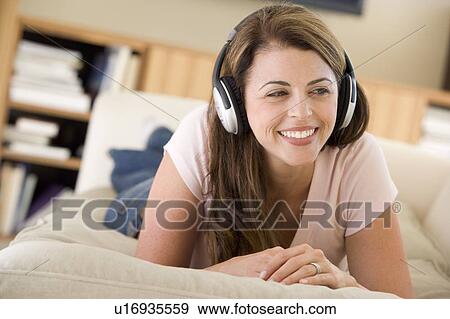 Woman in living room listening to headphones smiling View Large Photo Image Stock Photo - Woman in living room listening to headphones smiling. Fotosearch