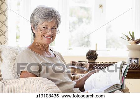Stock Photography - Woman in living room reading book smiling. Fotosearch