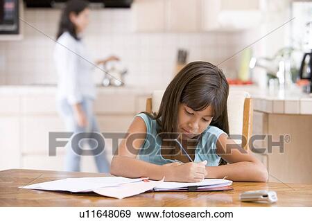 Young girl in kitchen doing homework with woman in background View Large Photo Image Stock Photo - Young girl in kitchen doing homework with woman in background. Fotosearch