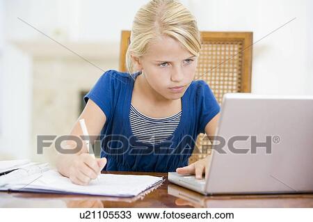 Stock Image - Young girl with laptop doing homework in dining room. Fotosearch