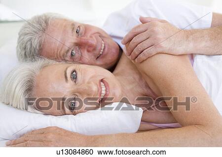 Stock Image - Couple lying in bed together smiling. Fotosearch