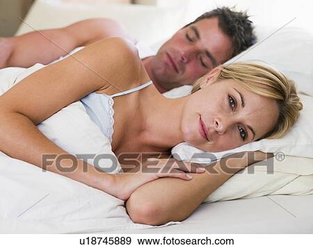 Stock Photo - Couple lying in bed with the man sleeping. Fotosearch