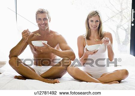 Couple sitting in bed eating cereal and smiling View Large Photo Image Stock Image - Couple sitting in bed eating cereal and smiling. Fotosearch