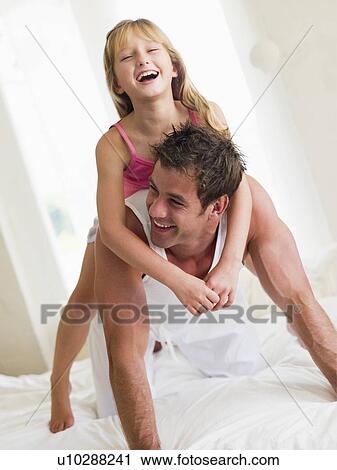 Stock Image - Man and young girl in bed playing and smiling. Fotosearch