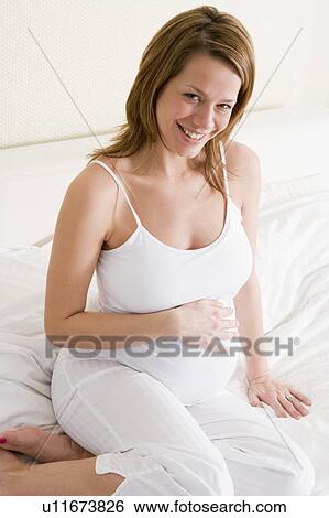 Pregnant woman sitting in bed smiling View Large Photo Image Stock Photograph - Pregnant woman sitting in bed smiling. Fotosearch