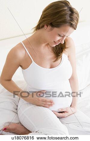 Stock Photograph - Pregnant woman sitting in bed smiling. Fotosearch
