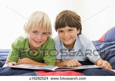 Two Young Boys Lying Down On A Bed Reading A Book View Large Photo Image Picture - Two Young Boys Lying Down On A Bed Reading A Book. Fotosearch