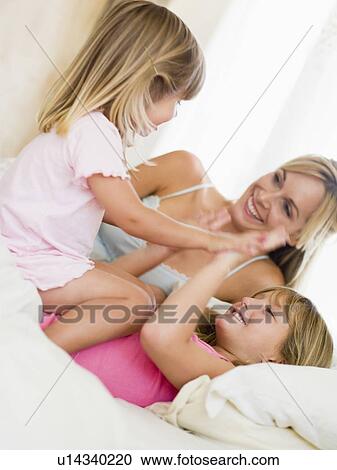 Woman and two young girls in bed playing and smiling View Large Photo Image Stock Image - Woman and two young girls in bed playing and smiling. Fotosearch