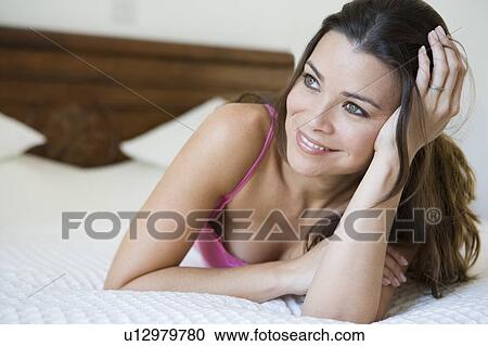 Stock Image - Woman relaxing on bed in bedroom smiling (selective focus). Fotosearch