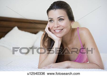 Stock Photograph - Woman relaxing on bed in bedroom smiling (selective focus). Fotosearch