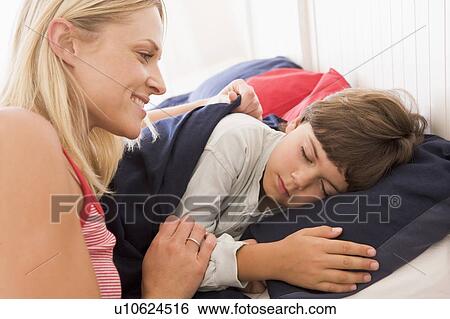 Stock Photograph - Woman waking young boy in bed smiling. Fotosearch