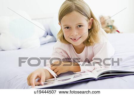 Stock Photo - Young Girl Lying On Her Bed In Her Pajamas, Reading A Book. Fotosearch