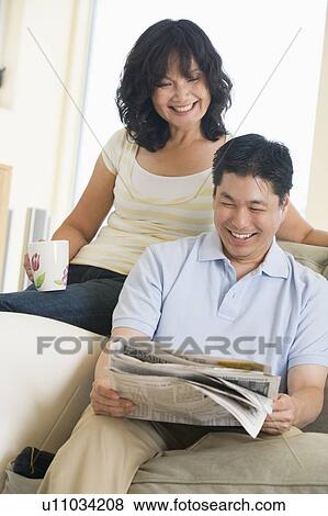 Couple relaxing with a newspaper and smiling View Large Photo Image Stock Photo - Couple relaxing with a newspaper and smiling. Fotosearch