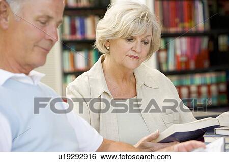 Stock Photograph - Man and woman in library reading (selective focus). Fotosearch