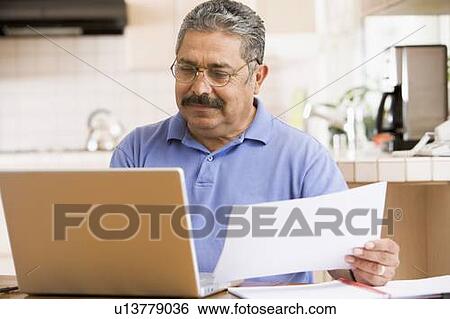 Man in kitchen with laptop and paperwork View Large Photo Image Stock Photograph - Man in kitchen with laptop and paperwork. Fotosearch