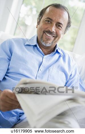 Stock Photography - Man in living room with newspaper smiling (high key/selective focus). Fotosearch