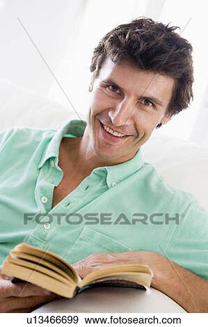 Stock Photo - Man reading book in living room smiling. Fotosearch