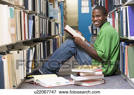 Stock Photo - Man sitting on floor in library holding book. Fotosearch