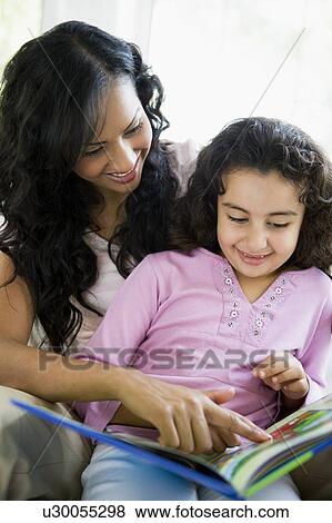 Stock Photo - Mother and daughter in living room with book smiling (high key). Fotosearch