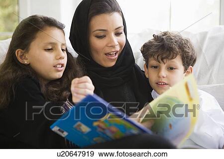 Stock Photo - Mother and two young children in living room reading book (high key/selective focus). Fotosearch