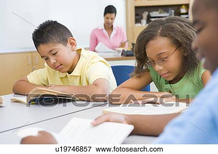 Stock Photo - Students in class reading with teacher in background (selective focus). Fotosearch