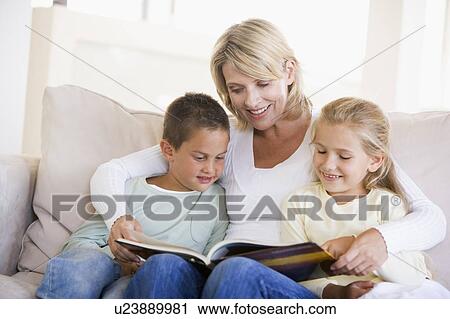 Stock Image - Woman and two children sitting in living room reading book and smiling. Fotosearch