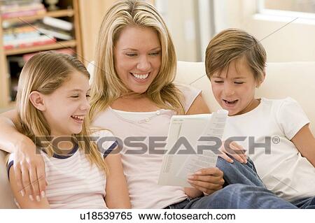 Stock Photography - Woman and two young children in living room reading book and smiling. Fotosearch