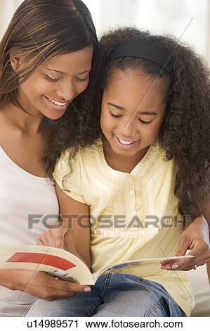 Woman and young girl sitting in living room reading book and smiling View Large Photo Image Stock Image - Woman and young girl sitting in living room reading book and smiling. Fotosearch
