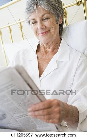 Stock Photo - Woman in bedroom with newspaper smiling. Fotosearch