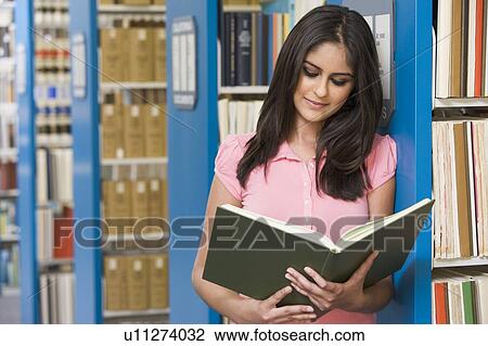 Stock Image - Woman in library reading book (depth of field). Fotosearch