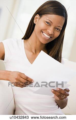 Stock Image - Woman in living room reading papers smiling. Fotosearch