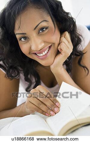 Stock Photo - Woman in living room with book smiling (high key/selective focus). Fotosearch