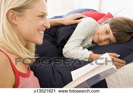 Stock Image - Woman reading book to young boy in bed smiling. Fotosearch