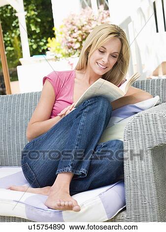 Stock Image - Woman sitting outdoors on patio with book smiling. Fotosearch
