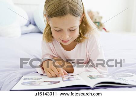 Stock Image - Young Girl Lying On Her Bed In Her Pajamas, Reading A Book. Fotosearch