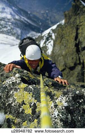 Stock Image - Mountain climber coming up snowy mountain smiling (selective focus). Fotosearch