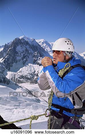 Stock Photograph - Mountain climber standing in snow on mountain warming up hands (selective focus). Fotosearch
