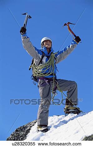 Stock Photography - Mountain climber standing on snowy mountain victorious and smiling. Fotosearch