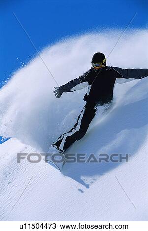 Stock Image - Snowboarder coming down snowy hill smiling. Fotosearch