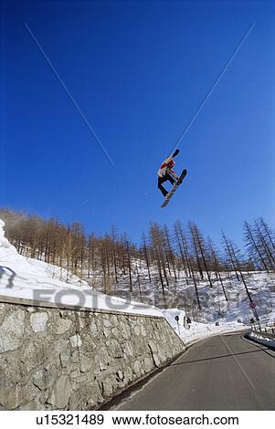 Snowboarder doing jump on snowy hill over a road (far away) View Large Photo Image Stock Photo - Snowboarder doing jump on snowy hill over a road (far away). Fotosearch