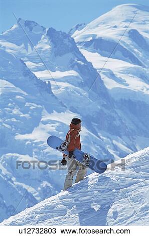 Stock Image - Snowboarder going up hill carrying board. Fotosearch