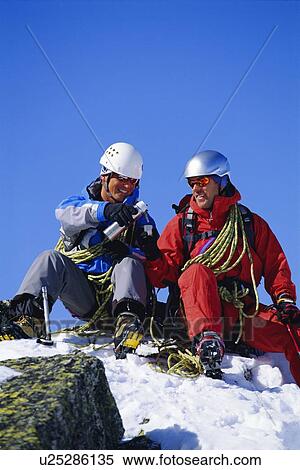 Two mountain climbers sitting on snowy mountain drinking from thermos and smiling (selective focus) View Large Photo Image Stock Photography - Two mountain climbers sitting on snowy mountain drinking from thermos and smiling (selective focus). Fotosearch