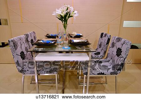 Stock Image - Place setting and bouquet of flowers on dining table and four chairs. Fotosearch