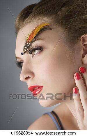Picture - Studio shot of teenage girl with makeup and feather on eyebrow. Fotosearch
