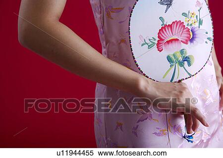 Stock Photography - Woman in Cheongsam holding fan, mid section. Fotosearch